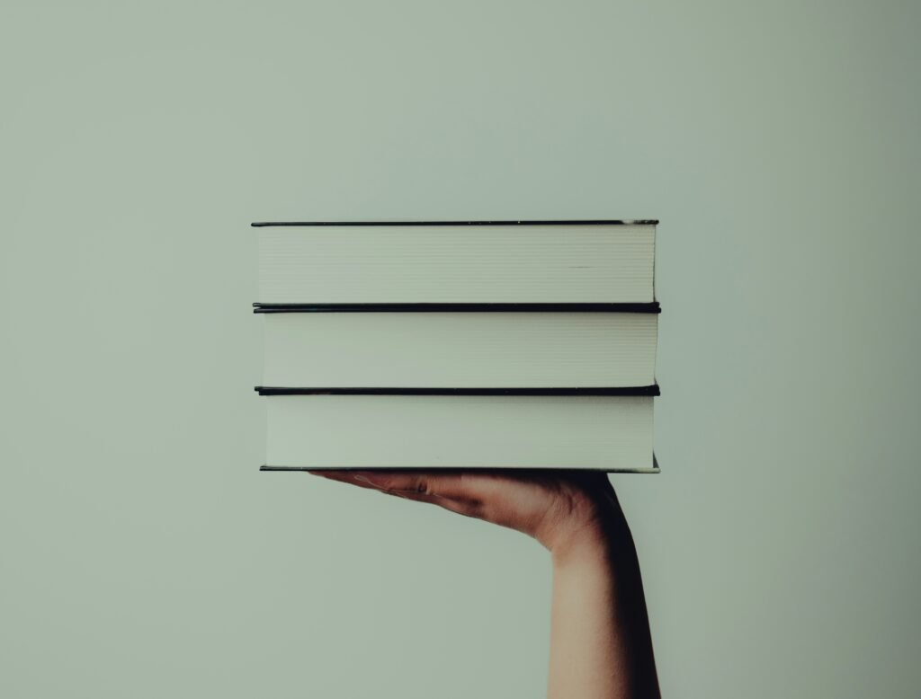 Een witte achtergrond met in het midden een hand met daarop 3 boeken. Je ziet de witte kant van de boeken. Het artikel gaat over boekentips voor iedereen die een huis wil kopen.